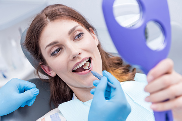 A woman looking at her healthy teeth in a mirror in a dentist’s chair.