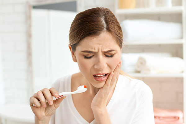 Woman with toothbrush holding her jaw in pain.