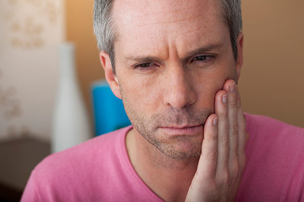 A man that needs tooth abscess treatment holding his jaw.