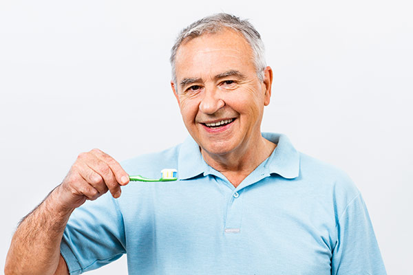 A man with gray hair smiles as he prepares to brush his aging teeth.