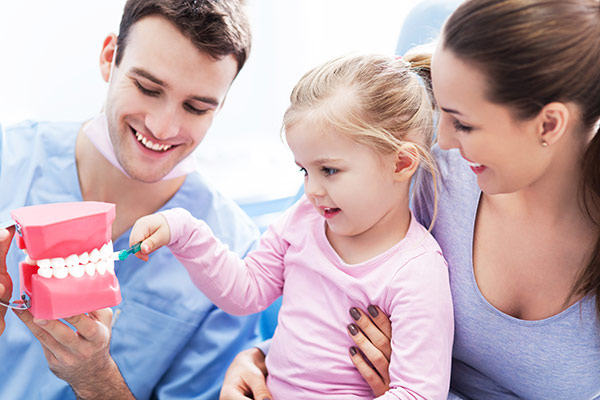 A dentist teaching a parent and her daughter about dental health for kids.