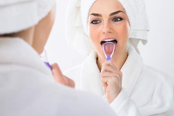 A woman learning how to clean her tongue with a tongue scraper.