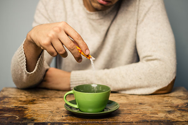 A man pouring artificial sweetener into his coffee.