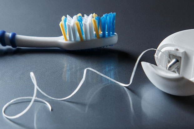 Close-up photo of teeth cleaning items, including the bristled end of a toothbrush and a short length of dental floss, unwound from its holder.