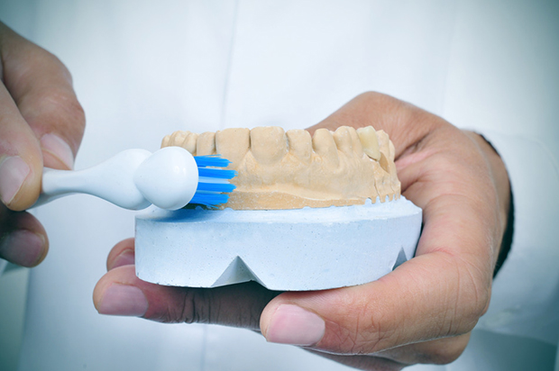 a young dentist man shows how to brush teeth with a toothbrush using a dentist mold in order to treat gum disease