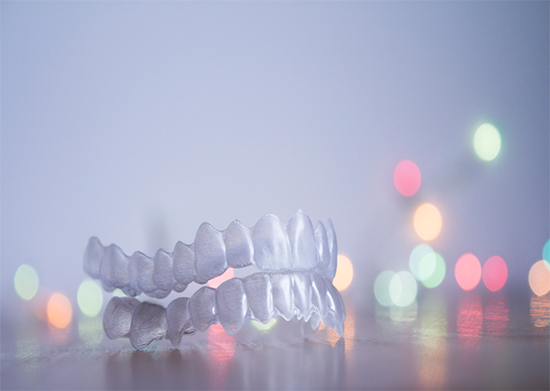 A set of upper and lower clear aligners against a background of colored lights - Alternatives to braces