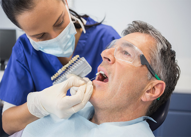 Dentist comparing teeth whitening results of her patient with that of a model tooth - getting teeth whitened