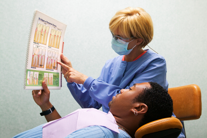 Dental hygienist shows a chart explaining periodontal disease to a patient.