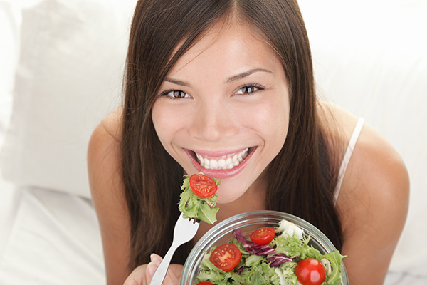 Best Food for Healthy Gums & Teeth | Happy woman smiling while eating a healthy salad with tomatoes.