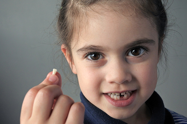 Young girl smiling while holding her missing tooth in her hand - Origins of the Tooth Fairy legend