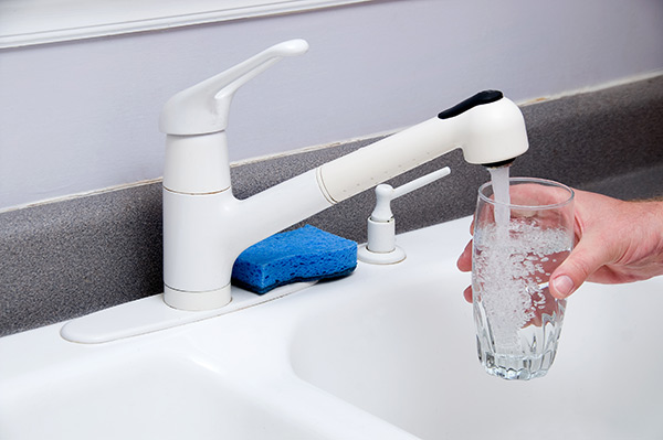 Person filling a cup with water from a kitchen faucet.