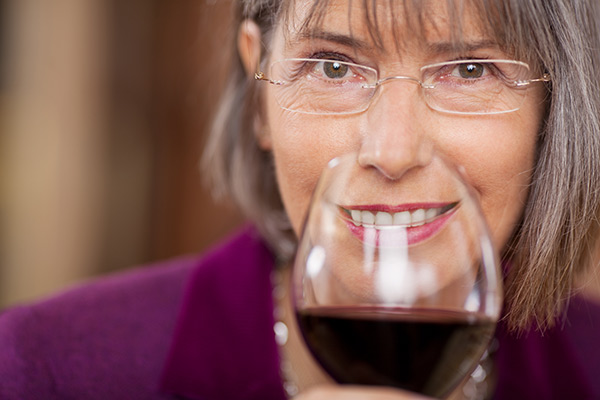 Woman smiling with white teeth behind glass of red wine.