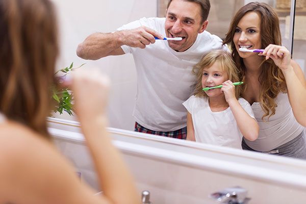 Family of three brushing their teeth together in the mirror.